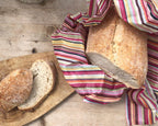 Loaves of bread wrapped in a colorful striped cloth on a wooden surface