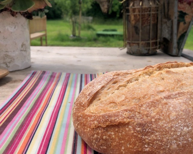 Loaf of bread on a colorful striped tablecloth with a garden in the background
