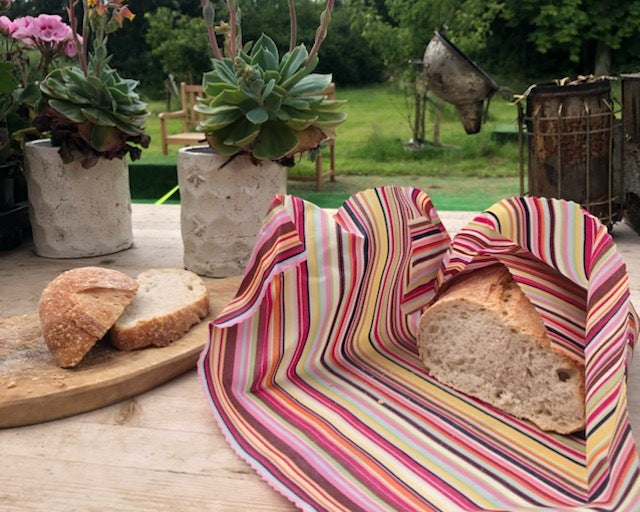 Striped reusable bread wrap with bread on a wooden table outdoors