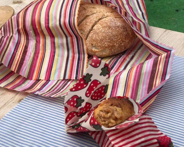Bread and a muffin in reusable fabric wraps on a striped surface