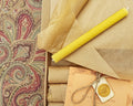 Rolls of brown paper and yellow candles on a patterned fabric background
