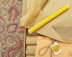 Rolls of brown paper and yellow candles on a patterned fabric background