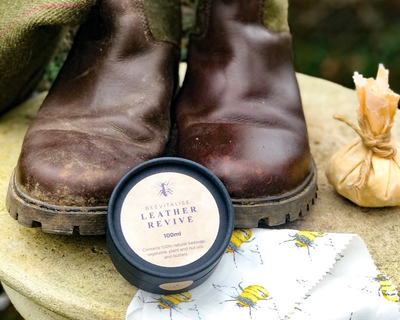 Pair of worn brown boots with a container of leather revive on a floral cloth.