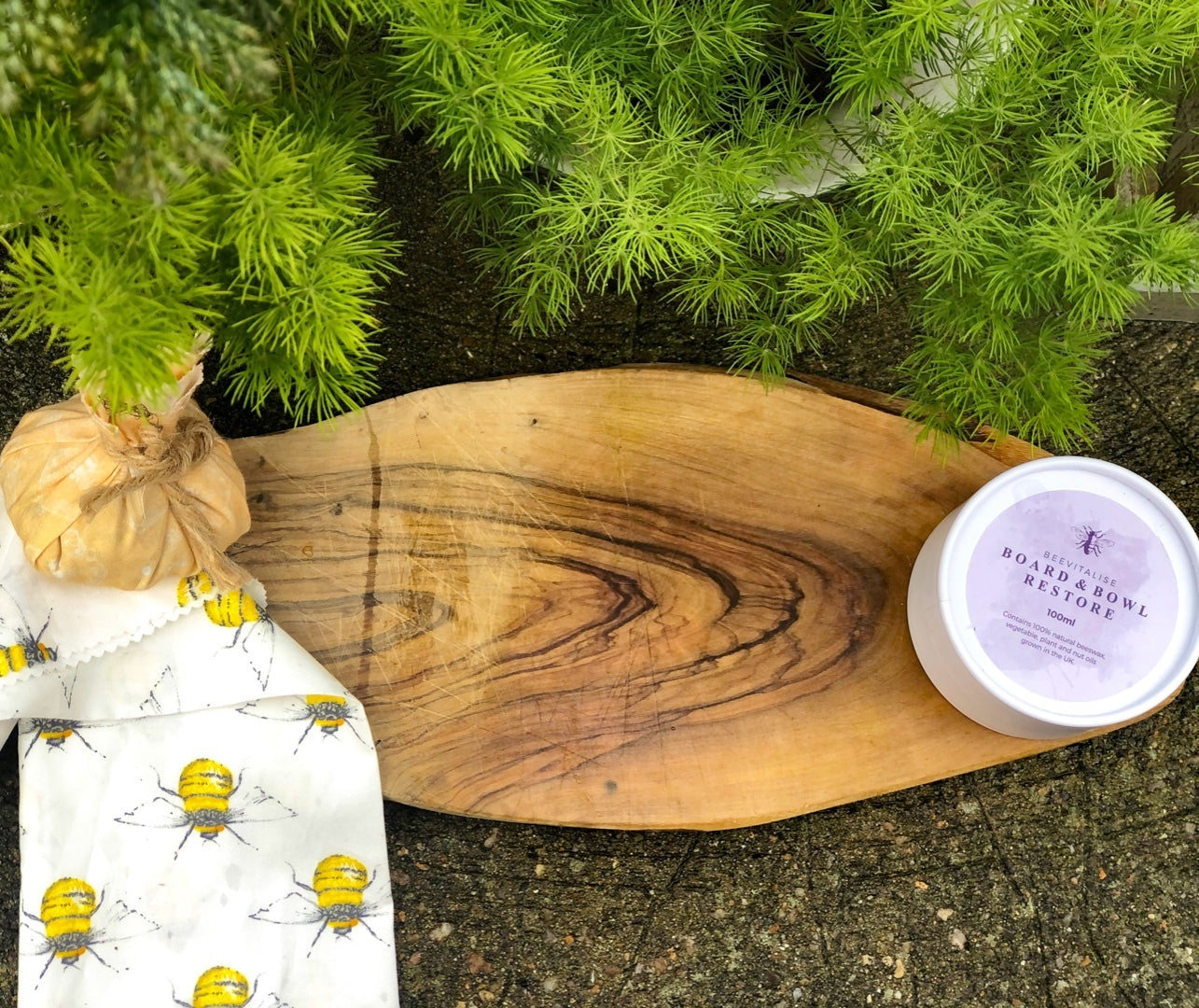 Wooden cutting board with a container of 'Bourgeoisie Beauty' product on a stone surface with greenery in the background.