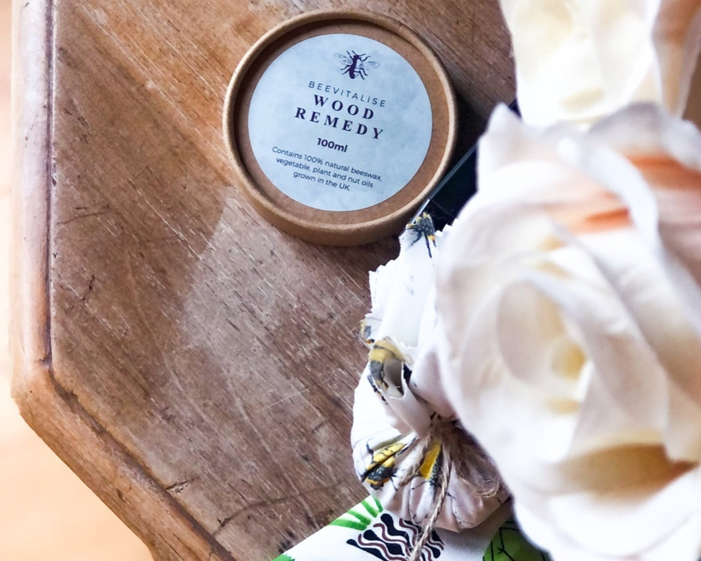 Wood remedy container on a wooden surface with a scrunchie and flowers.
