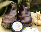 Pair of worn brown boots with a container of leather revive cream on a stone surface.