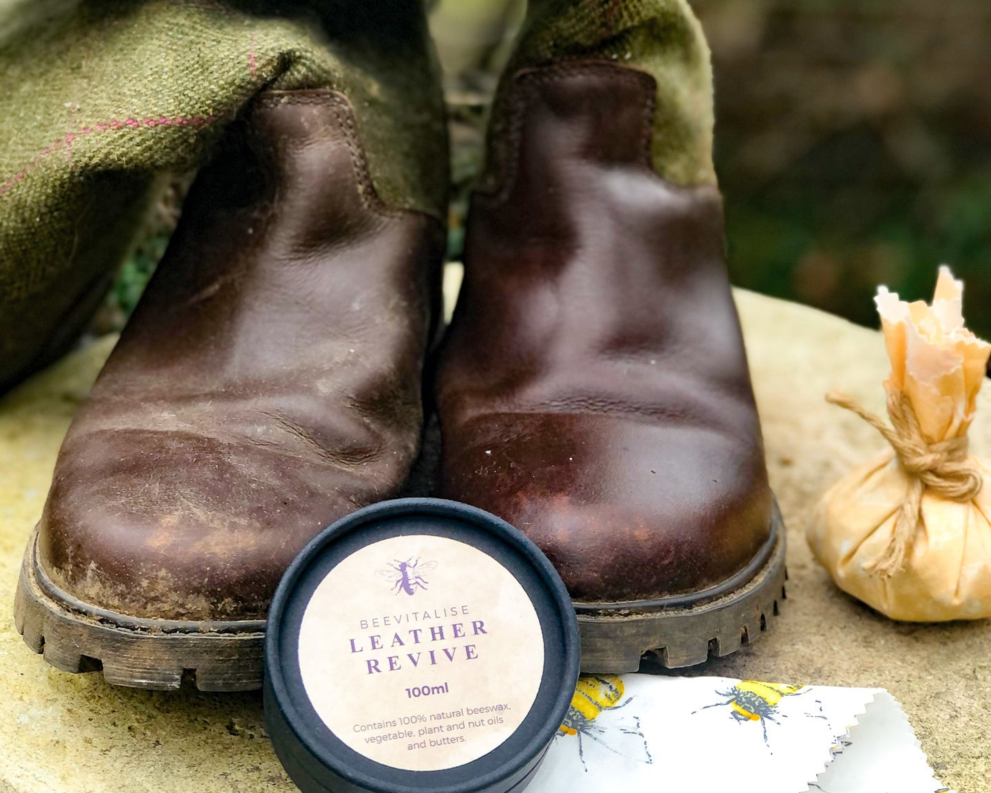 Pair of worn brown boots with a container of leather revive cream on a stone surface.